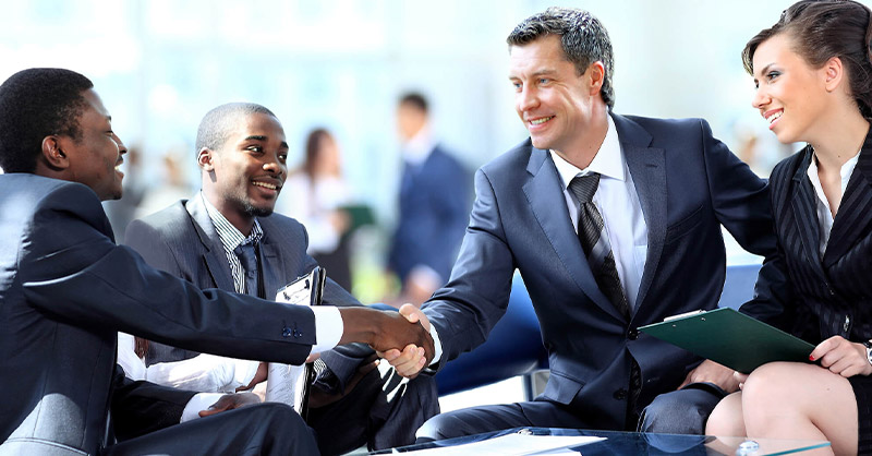 Image de personnes en costume discutant et se serrant la main avec le sourire lors d'une réunion d'affaires.